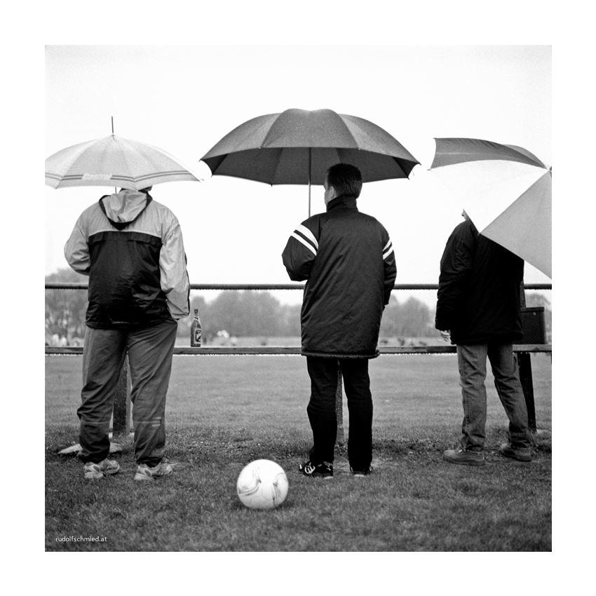 Drei Fußballfans mit Regenschirm von hinten