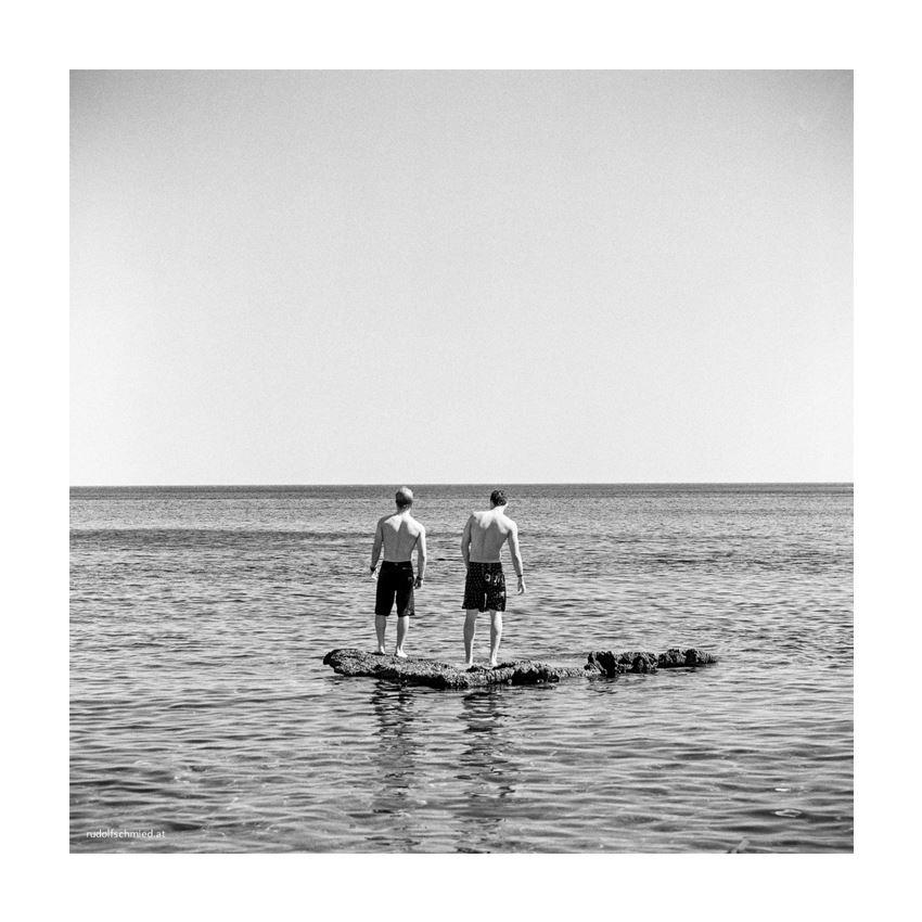 Zwei junge Männer auf einem Felsen im Meer