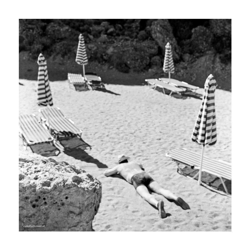 Ein Mann liegt im Sand zwischen Sonnenschirmen