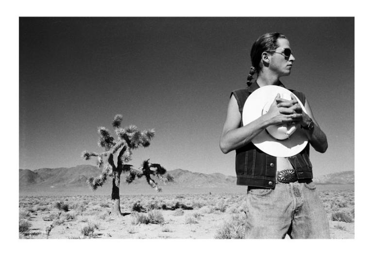 Ein Mann mit einem Cowboyhut vor der Brust posiert neben einem Joshua Tree