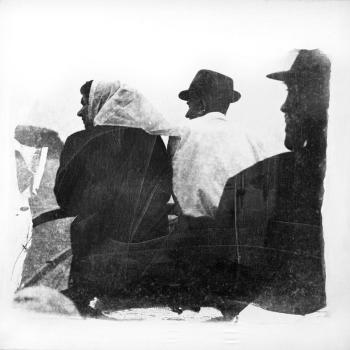 Zwei Männer mit Hut und eine Frau mit Kopftuch von hinten fotografiert